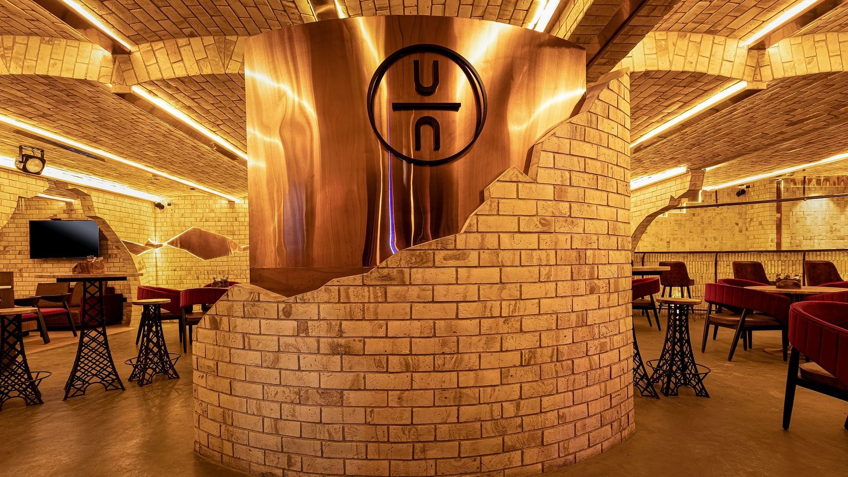 The Underground Bar restaurant interior with warm lighting, brick walls, and a large copper feature displaying a logo. Tables and chairs are neatly arranged
