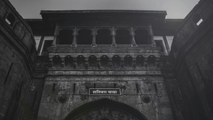 A stone gateway with an arched entrance, balconies with railings above, and a signboard mounted over the arch against the sky.