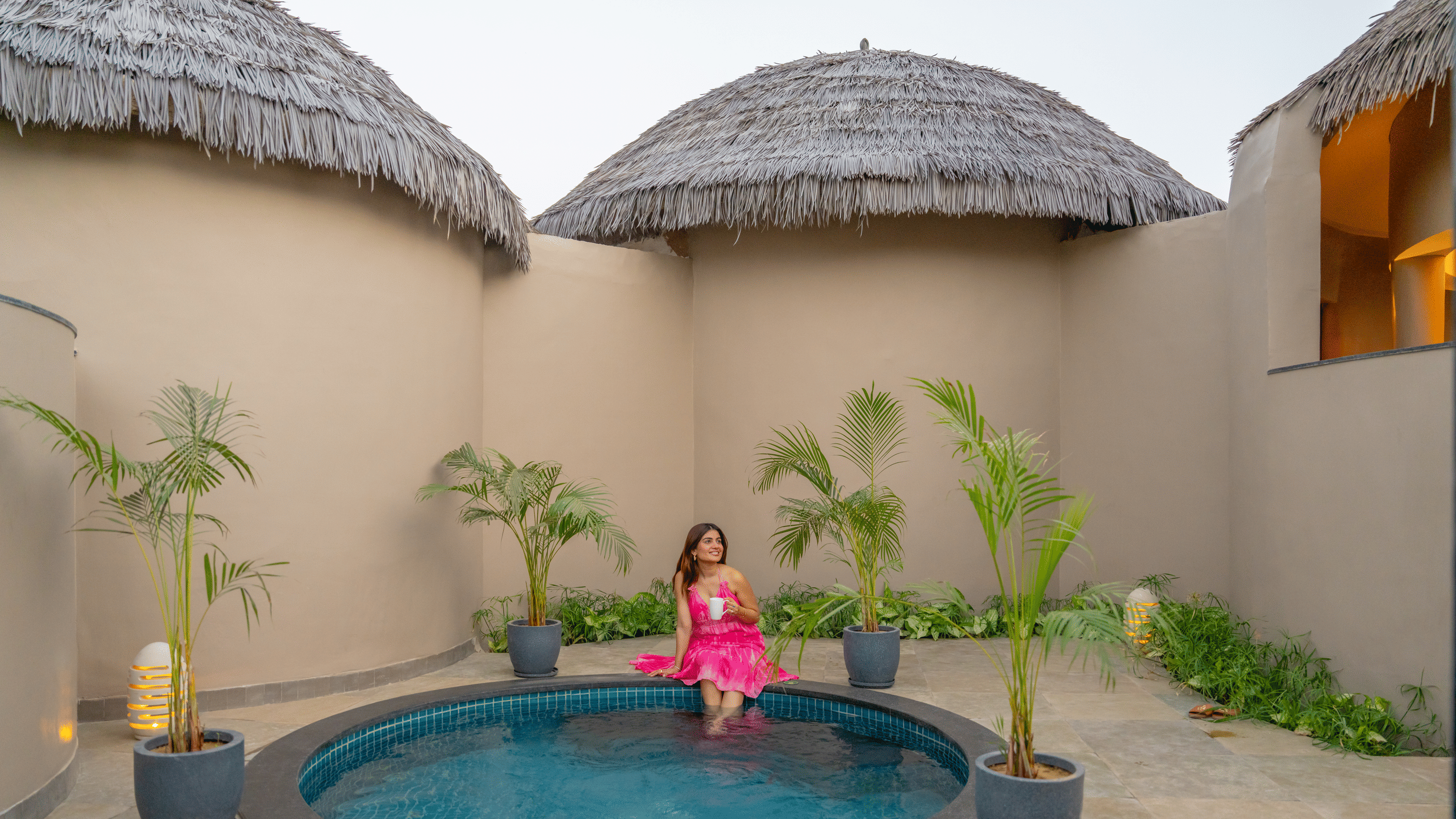 A private plunge pool courtyard with a woman in pink attire, surrounded by thatched-roof cottages at Ananta Spa and Resort, Ajabgarh.