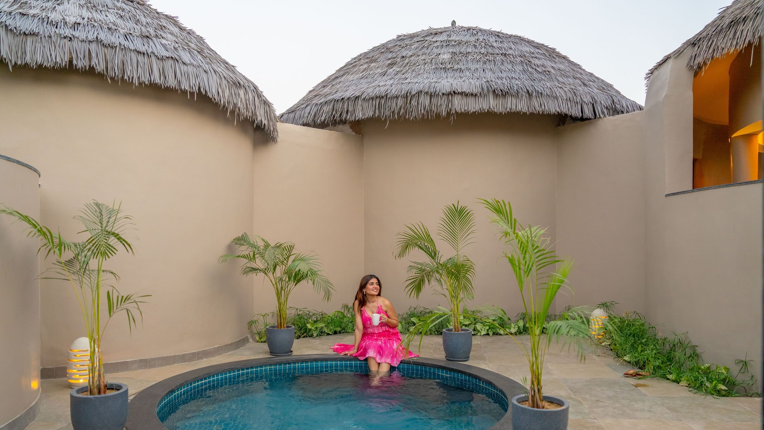 A private plunge pool courtyard with a woman in pink attire, surrounded by thatched-roof cottages at Ananta Spa and Resort, Ajabgarh.