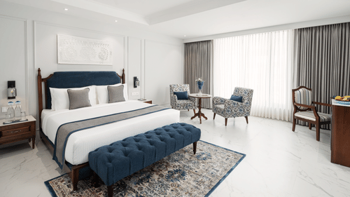 A spacious room with a large bed, carpeted floors, furniture, a work desk, and blackout curtains - MJ Sarovar Portico, Haridwar