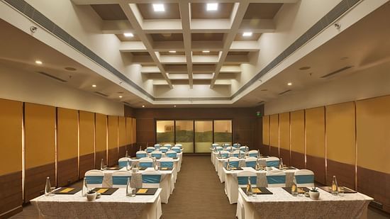 Modern conference room with rows of tables, blue and white chair covers, and a structured ceiling - Heritage Village Resorts & Spa.