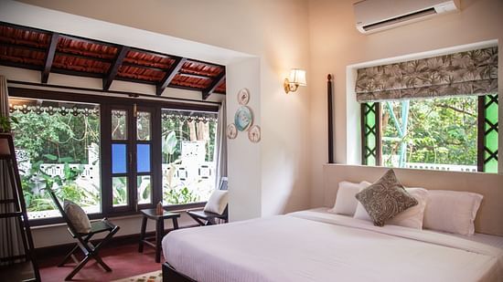 An image of a bed with big windows on the side with greenery outside at Lamrin Ucassaim Hotel, Goa