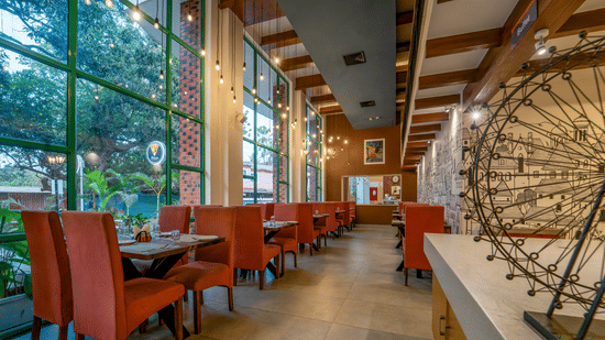 Modern restaurant interior with terracotta chairs, pendant Edison bulbs, floor-to-ceiling windows, and a city mural wall.