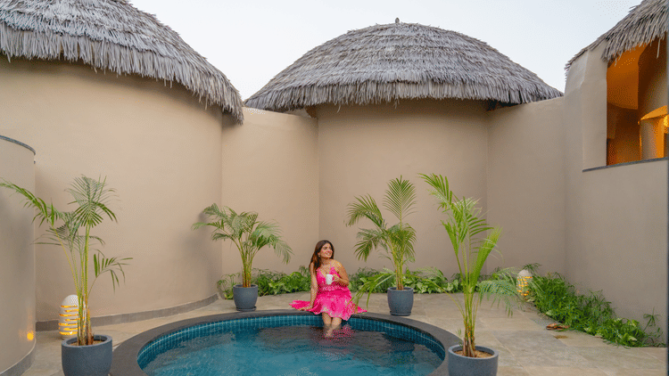 A private plunge pool courtyard with a woman in pink attire, surrounded by thatched-roof cottages at Ananta Spa and Resort, Ajabgarh.