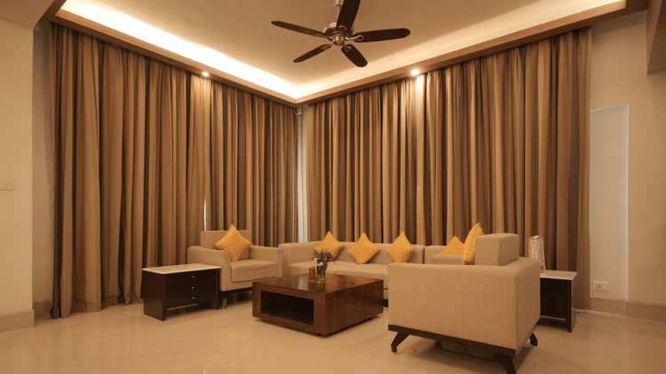 A living room with comfortable sofas, a center table, floor-to-ceiling curtains, and warm lighting in the Presidential Suite at Clarks Amer, Jaipur.