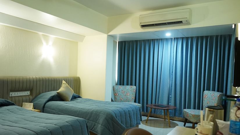 An image of a bedroom with twin beds, AC, table and chair, and two single sized sofa