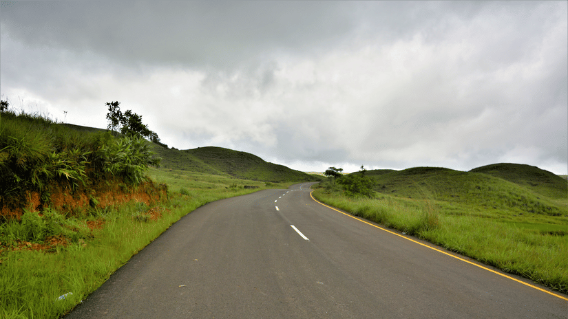 Empty asphalt road curving between bright green rolling Khasi hills under a heavy grey monsoon sky in the Cherrapunji region of Meghalaya.