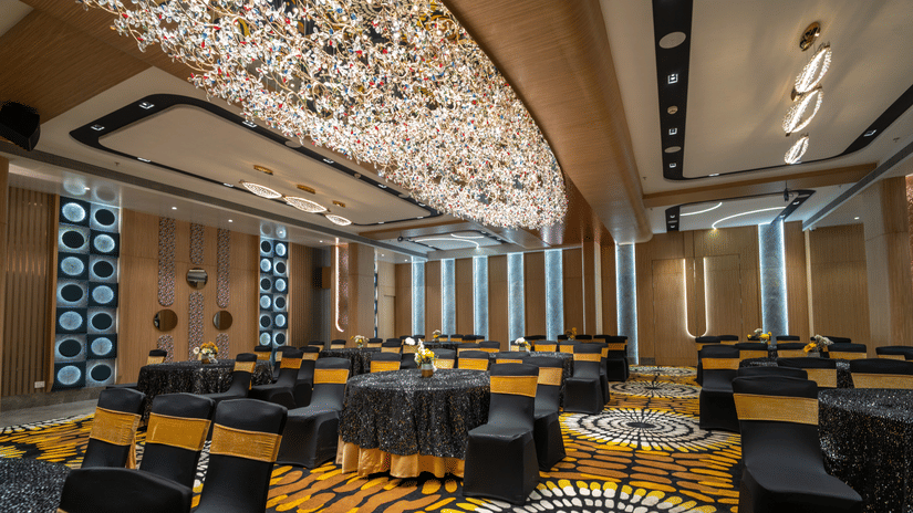 A banquet hall featuring neatly arranged cluster style seating arrangement, carpeted floors and a grand linear chandelier | Pride Elite Chhatrapati Sambhajinagar