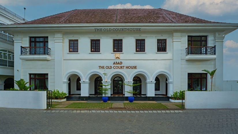 A colonial-style white building with a symmetrical facade, arched entryway, and a sign reading The Old Court House above the entrance