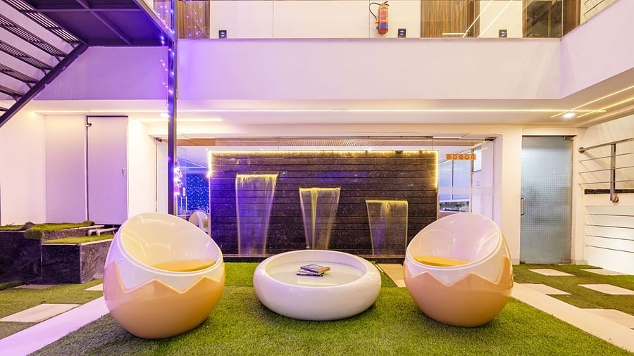 Outdoor seating area featuring broken egg-shaped chairs, artificial grass-flooring, and water fountains in the background at Hotel Bawa, Gurgaon.