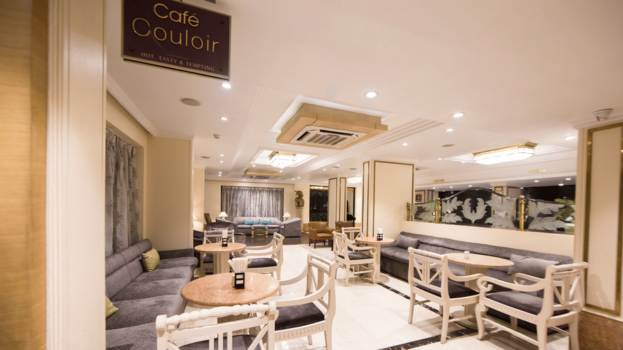 Cafe Couloir at Hotel Bawa International, Vile Parle featuring a dining area with couch and sofa chairs with tables in each setting.