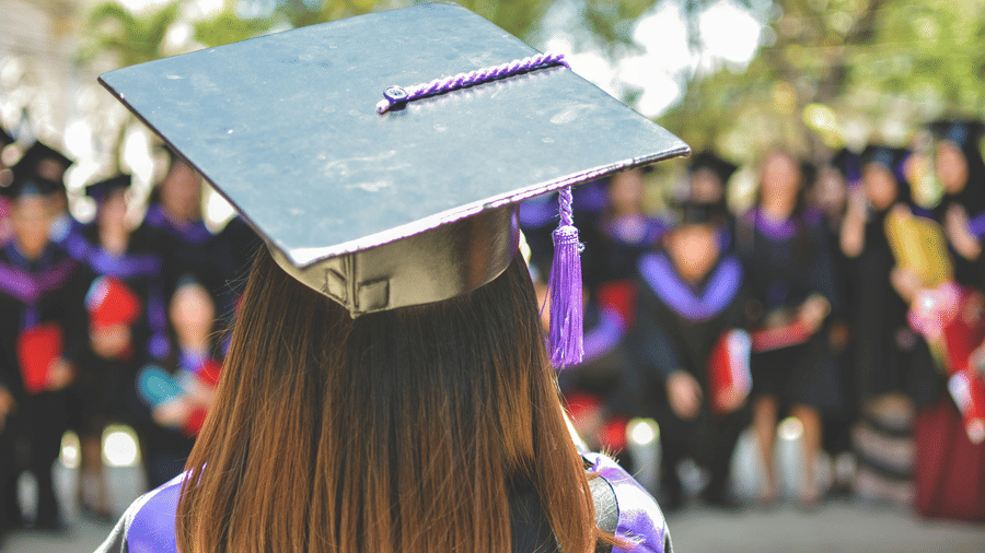 A girl in a black cap and gown faces a crowd during a graduation ceremony