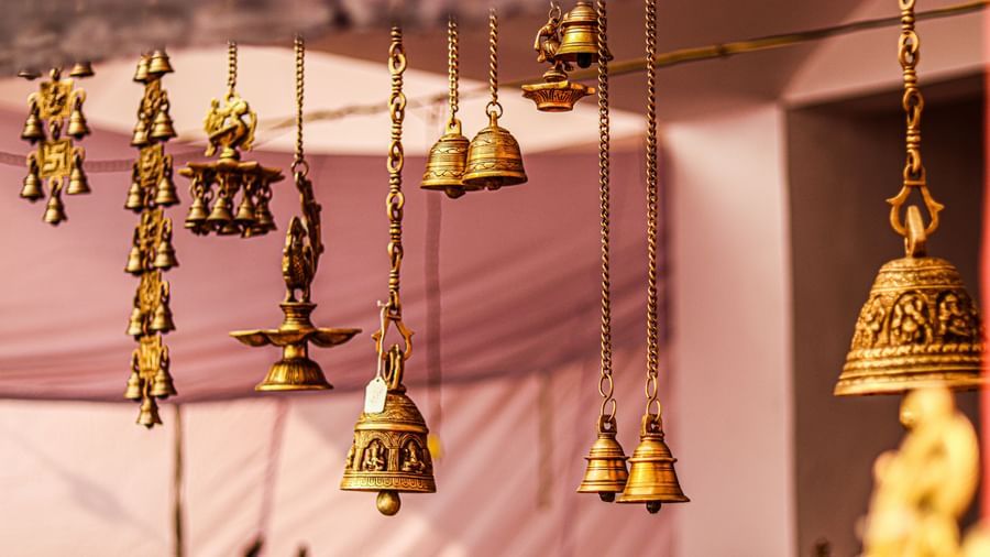 A selection of traditional Indian brass bells and lamps hang from chains, displayed at a market stall