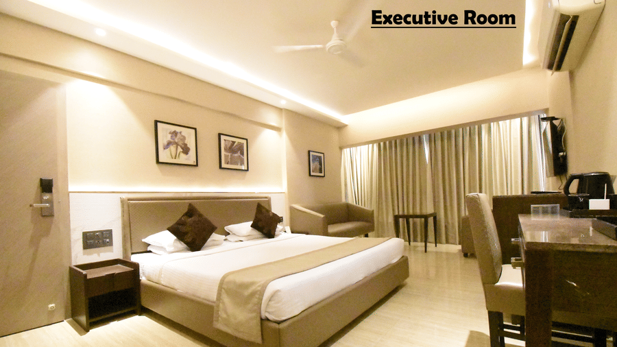 A well-decorated bedroom at Kings International Juhu featuring a bed, a bedside table, paintings on walls, and full-length opaque curtains. 