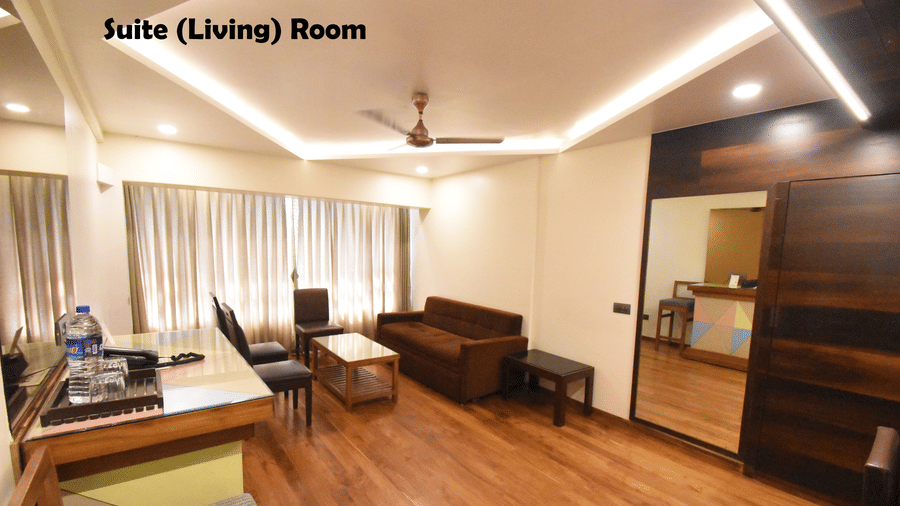 The living area of a Suite Room at Kings International Juhu featuring a sofa and 3 chairs facing a coffee table,  a ceiling fan and modern lighting.