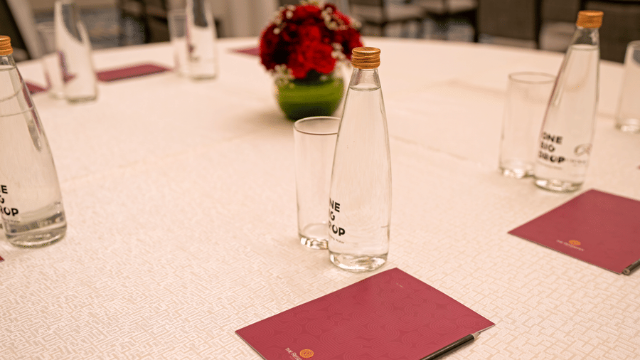 Close-up of a white round table at The Residency Signature Madurai set with glass water bottles, small notebooks, and a flower arrangement.