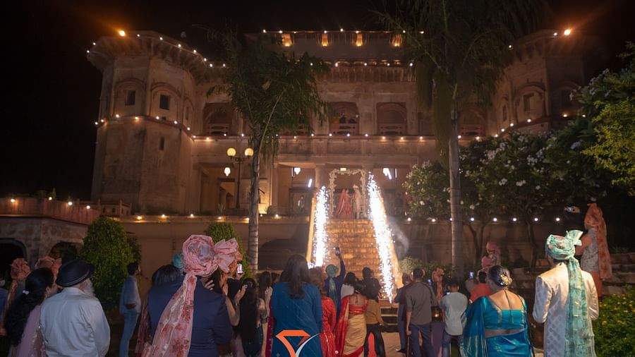 Guests are gathered outside the illuminated Tijara Fort-Palace - 19th Century, Alwar at night, with a red carpet leading up to the building where sparklers are going off.