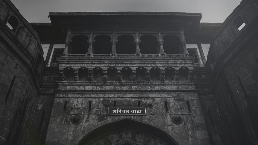 A stone gateway with an arched entrance, balconies with railings above, and a signboard mounted over the arch against the sky.