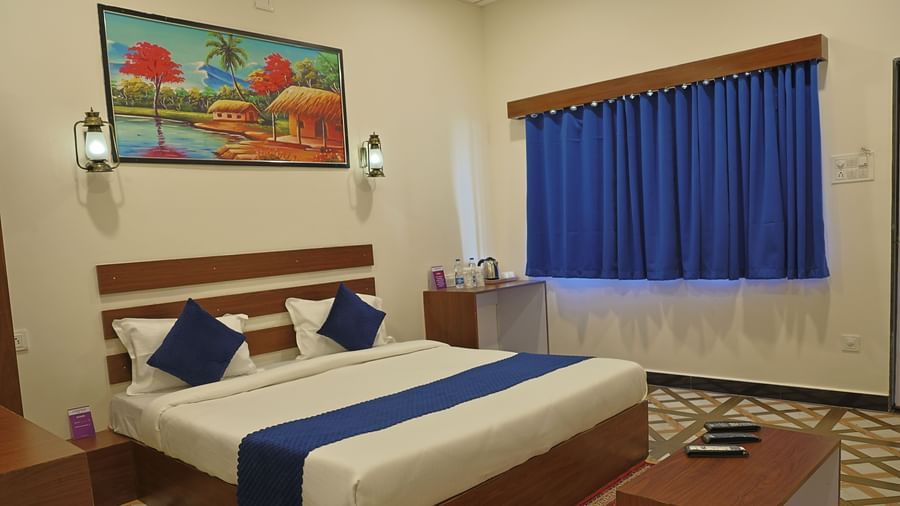Interior of a room at VITS Select Diamond Resort, Sasan Gir with a double bed, side table, painting, and curtains.