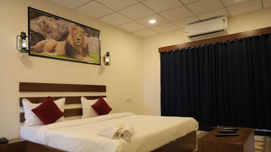 VITS Select Diamond Resort, Sasan Gir room with a double bed, side tables, red cushions, wall lamp, and painting above the headboard.