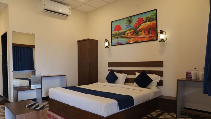 Interior of a room at VITS Select Diamond Resort, Sasan Gir with a double bed, side table, painting, and curtains.