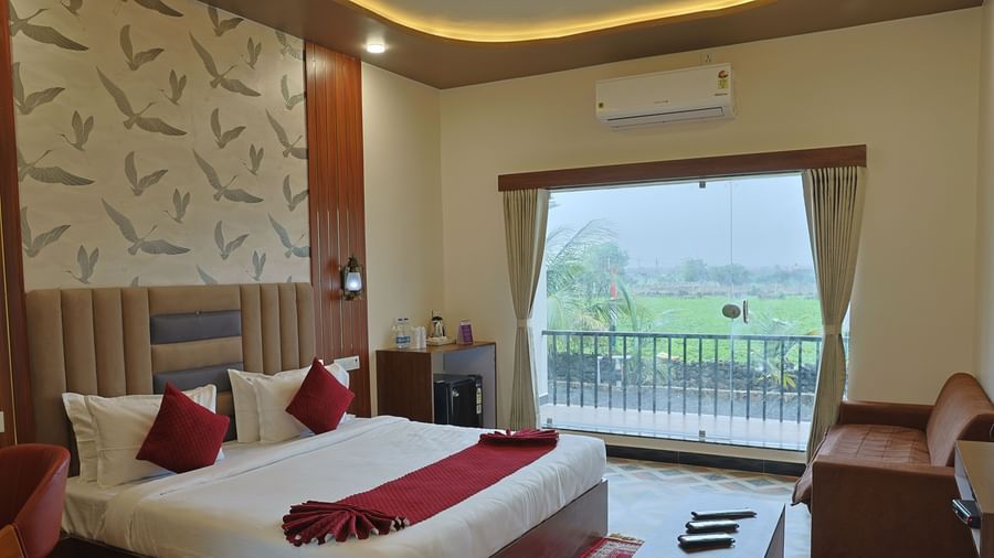 An Executive Room at VITS Select Diamond Resort, Sasan Gir. It includes a bed with a red bed runner, a small sofa, a ceiling fan, and a balcony.