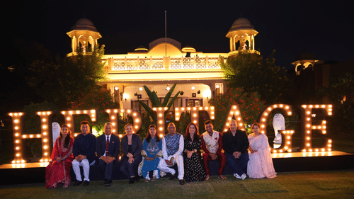 Guests gathered for a group photo in front of the iconic illuminated 'Heritage' sign at a nighttime celebration.
