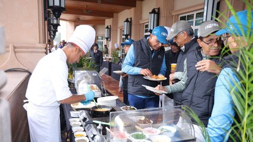 An image of a group of people gathered near a food counter where one person is severing food to the rest of the guests at Heritage Village Resorts & Spa