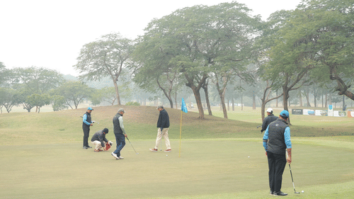 A wide outdoor space with trees and a distant landscape and people playing golf.- Heritage Village Resorts & Spa