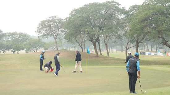 A wide outdoor space with trees and a distant landscape and people playing golf.- Heritage Village Resorts & Spa