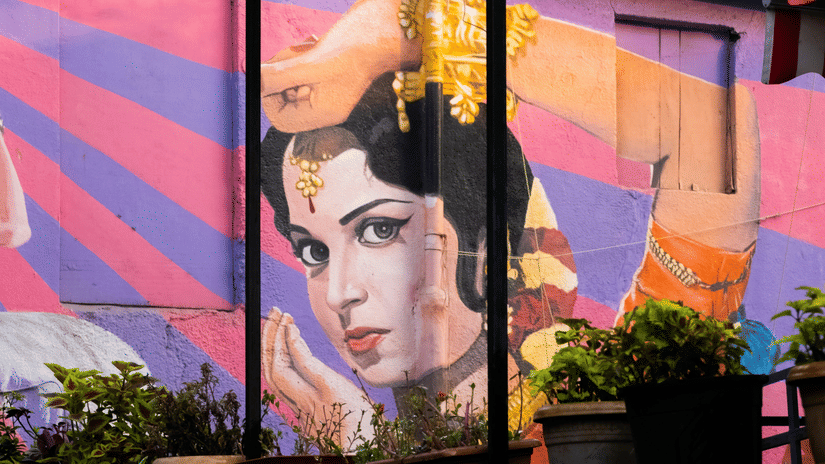 A colourful wall mural depicting a traditional Indian classical dancer with expressive eyes, ornate jewellery, and graceful hand gestures against a vibrant backdrop.