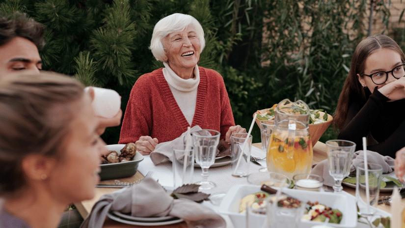 Family gathered around an outdoor dining table, sharing a joyful meal with drinks and laughter