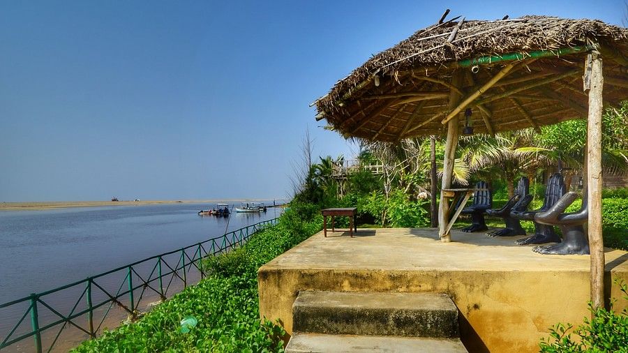A thatched-roof gazebo overlooking a tranquil river, offering a peaceful spot for reflection and relaxation amidst lush greenery.