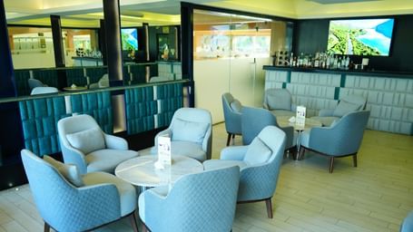 Lounge seating with armchairs and tables beside large glass windows at Grande Bay Resort & Spa.