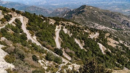 A winding paved road snaking up a mountainside covered in trees and shrubs.