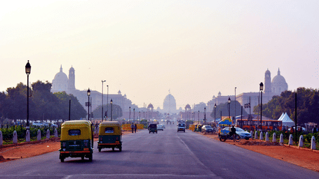 A picture of the Kartavya Path in  delhi with a view of the Rashtrapati Bhavan in the front. There are two yellow and green autos driving on this path with other cars in the background.