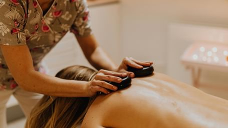 Therapist giving a hot stone back massage to a woman lying on a spa bed in a relaxing setting.