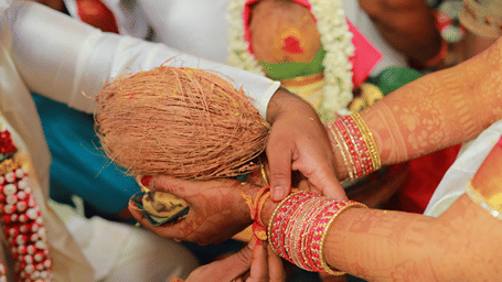 Hands hold a ceremonial coconut adorned with sacred thread during traditional wedding rituals.