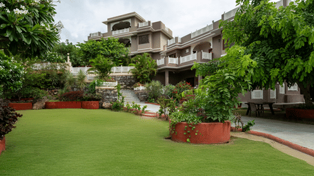 A manicured green lawn surrounds a multi-storey hotel property framed by lush tropical trees.