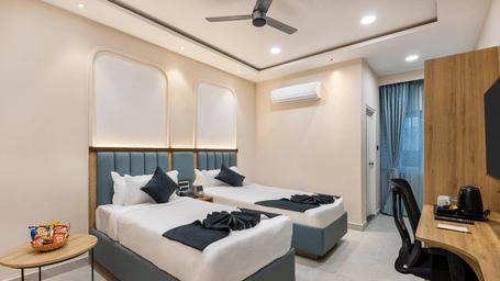 2 single beds with white bedding, a desk with an office chair, and a ceiling fan, at Monday Hotels & Suites Madhapur Hyderabad.