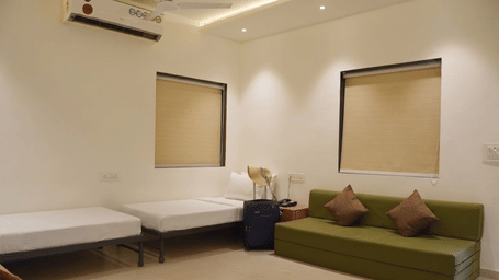 A living room at Oceanature Resort, Alibaug features 2 single beds, a green sofa with brown pillows, and 2 window shades.