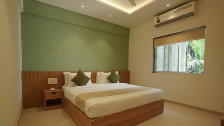 A bedroom with a king size bed, side table, and an air-conditioners at Oceanature Resort, Alibaug.