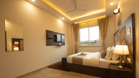 A bedroom with a king size bed, side tables, lamps, wall art, and a wall mounted television at Perfectstayz Value Dhruv Nanda, Haridwar.