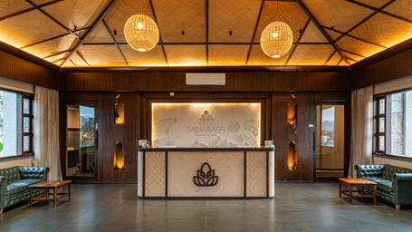 A grand wooden reception desk sits in a spacious lobby featuring a vaulted ceiling and warm ambient lighting - Sajjan Bagh Resort and Spa, Kumbhalgarh