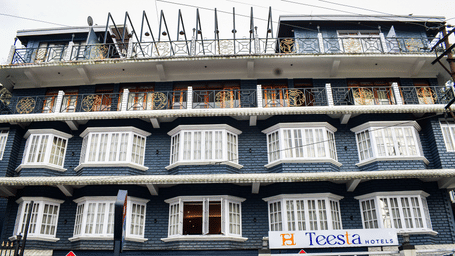 The front facade of Teesta Hotel, Kalimpong displays rows of windows across multiple storeys. Signs for businesses are positioned at the bottom of the building.