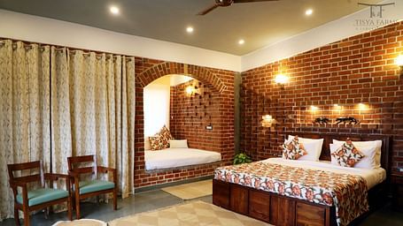 A bedroom at Tisya Farms, Gurgaon with a double bed, chairs, brick walls, curtains, and overhead lighting.