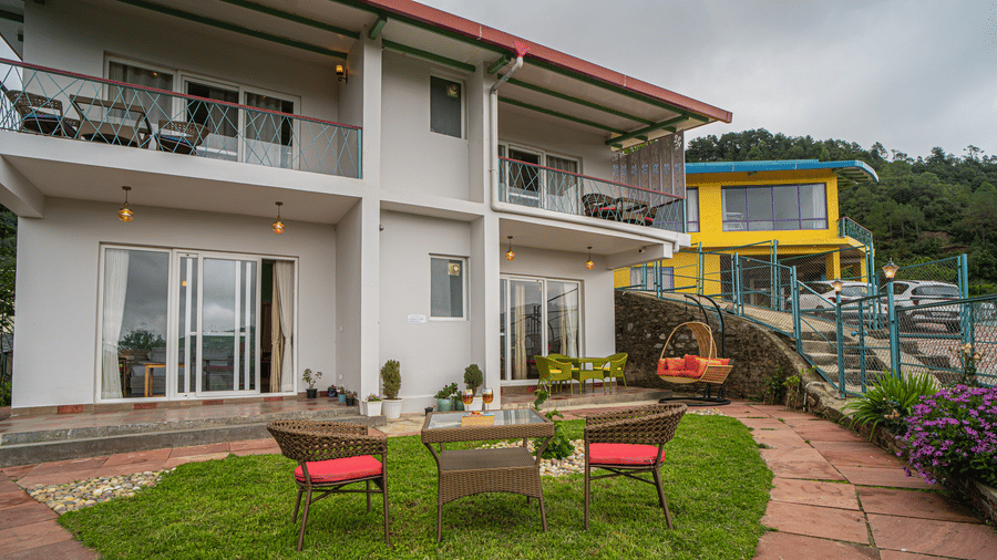 A balcony with a lawn, chairs, and a pathway leading to the entrance at Adrushya Estates, Mukteshwar.