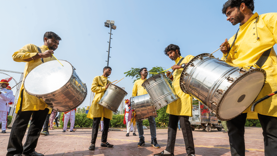 Performers in yellow Kurtas play traditional metal drums outdoors during an event at Garh Govind.