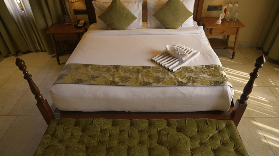 A white bed with green cushions and a green tufted bench at the foot of the bed at Hotel Sonar Bangla, Sundarban.